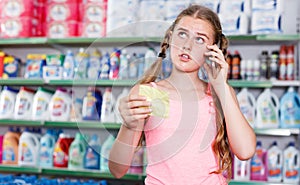 serious girl standing in store choosing products while talking by phone and looking at shopping list