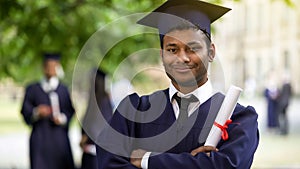 Serious graduate crossing arms with diploma in hand, completion of studies pride