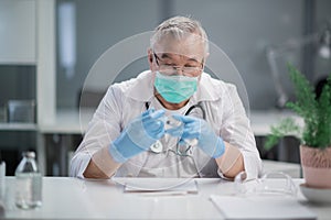 A serious, gray-haired doctor fills a syringe with a vaccine from a glass ampoule to vaccinate his patient against the