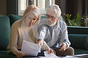 Serious grey haired mature couple calculating bills, checking finances together