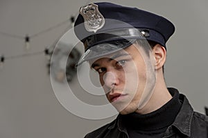 A serious guy of 20-25 years old in a police cap on the background of a New Year`s wreath, a light background.