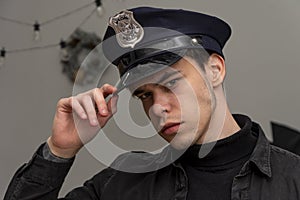 A serious guy of 20-25 years old in a police cap takes a visor on the background of a New Year`s wreath, a light background.