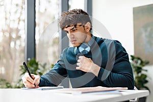 Serious guy doing his home assigment looking attentively in copybook and writing info, sitting in university audience photo