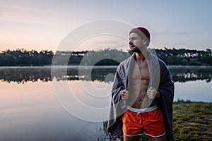 Serious guy at the forest near the water and preparing for the swimming in the cold lake at morning