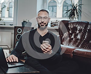 Serious guy with mobile phone and laptop looking at camera