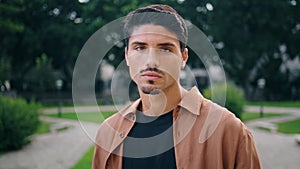 Serious guy posing park portrait. Young man face looking camera standing nature