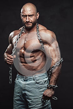 Serious and handsome guy poses in dark background with heavy chains