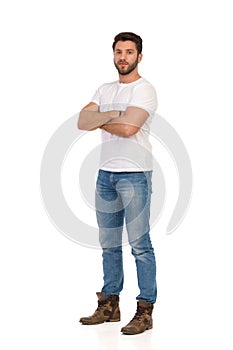 Serious Handsome Man In Jeans And White T-shirt Is Standing With Arms Crossed