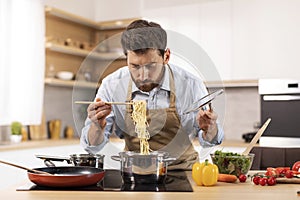 Serious handsome mature caucasian man with beard in apron prepare pasta in minimalist kitchen interior