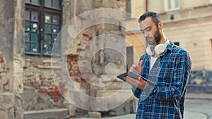 Serious Handsome Tourist Walking on Street Using Digital Tablet in Hands. Handsome Caucasian Man Texting, Scrolling Apps