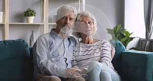 Serious happy senior couple bonding looking at camera on sofa
