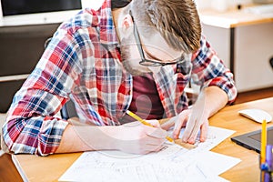 Serious hardworking student sitting at the desk and drawing blueprint