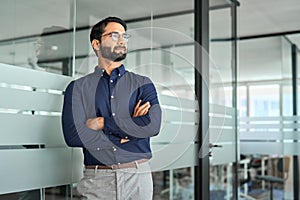 Serious Indian business man looking away standing arms crossed in office.