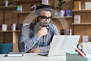 Serious indian business man working or studying on laptop computer.