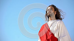 Serious Jesus Christ in white robe looking at humanity from heaven, religion