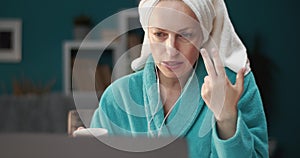 Serious lady in bathrobe and earphones having video call