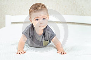 Serious little baby crawling on the bed on a white sheet in the parents bedroom. Close up portrait of newborn baby