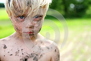 Serious Little Boy Covered in Dirt and Mud Outside