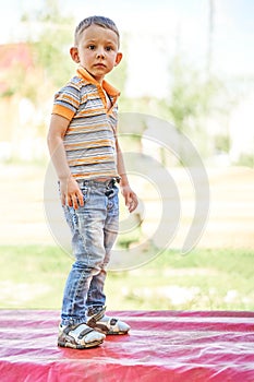 Serious little boy stands on bench on blurred background