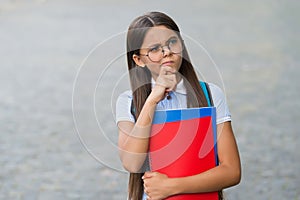 Serious little kid in glasses hold school books with thoughtful look outdoors, imagination