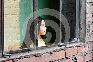 Serious little latin girl standing near window.