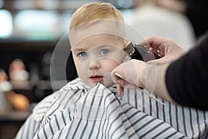 Serious and little scared cute blond baby boy with blue eyes in a barber shop having washing head by hairdresser.