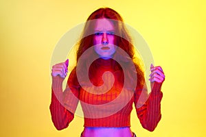 Serious lookin girl standing with fists up and looking at camera against yellow studio background in neon light