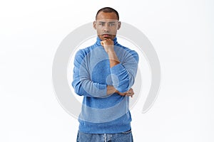 Serious-looking confident african-american businessman in blue turtleneck listening to employee report, watching