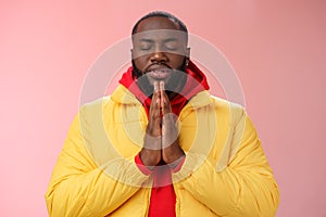 Serious-looking faithful young determined african-american praying guy in yellow coat press palms together pray close