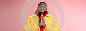 Serious-looking faithful young determined african-american praying guy in yellow coat press palms together pray close