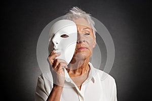 Serious older woman revealing face behind mask photo