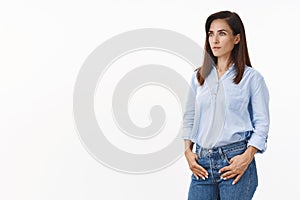 Serious-looking pretty adult trendy 30s woman standing half-turned empowered, confident pose, hold hands pockets, look