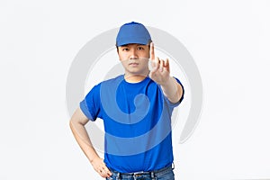 Serious-looking reluctant asian courier in blue uniform forbid something, disapprove behaviour or action, shaking finger