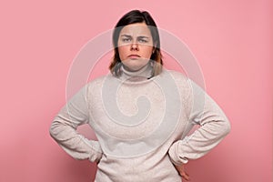 Serious looking woman with her hands on her hips against pink background