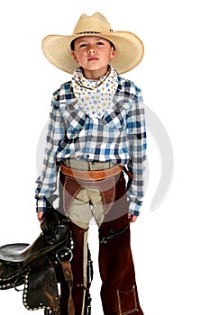 Serious looking young cowboy holding a saddle in c