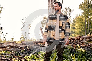 Serious lumberjack works in summer forest. Lumberjack with an ax in the evening.