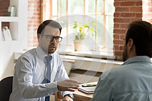 Serious male colleagues discuss business seated at workplace desk