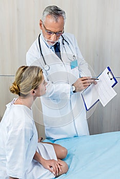 serious male doctor with stethoscope over neck pointing at clipboard to female patient in hospital