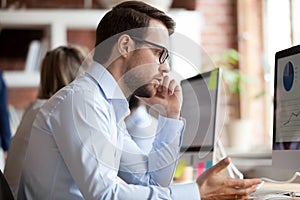 Serious male employee talking by phone at workplace