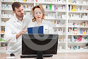 Serious male and female pharmacists standing behind the counter in a pharmacy, discussing