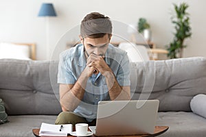 Serious male looking at laptop screen thinking