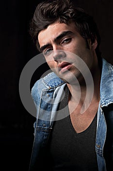 serious male model posing in blue jacket on dark shadow bac