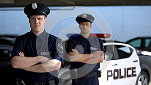 Serious male officers standing with hands crossed against police car background