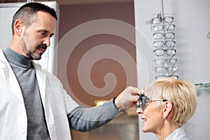 Serious male optometrist examining mature woman, determining diopter in ophthalmology clinic