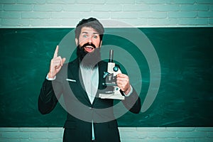 Serious male Student studying in school. Young bearded teacher near chalkboard in school classroom. Teachers day -