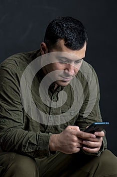 A serious man 30-35 years old is typing in a smartphone on a black background.