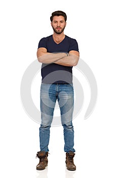 Serious Man In Boots, Jeans And Blue T-shirt Is Standing With Arms Crossed