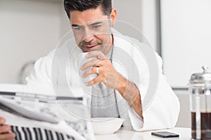 Serious man with coffee cup reading newspaper in kitchen photo