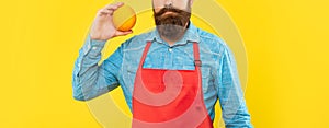 Serious man crop view in red apron holding fresh orange citrus fruit yellow background, fruiterer photo