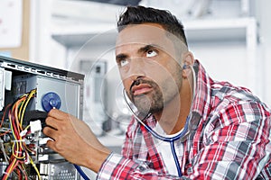 Serious man examines computer with stethoscope